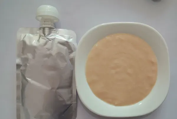 Spouted pouch of chicken puree pet food beside a dish of the contents