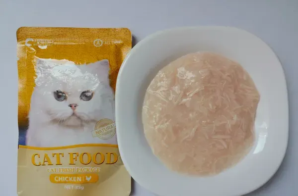 Shredded chicken soup cat food pouch beside a shallow dish of broth