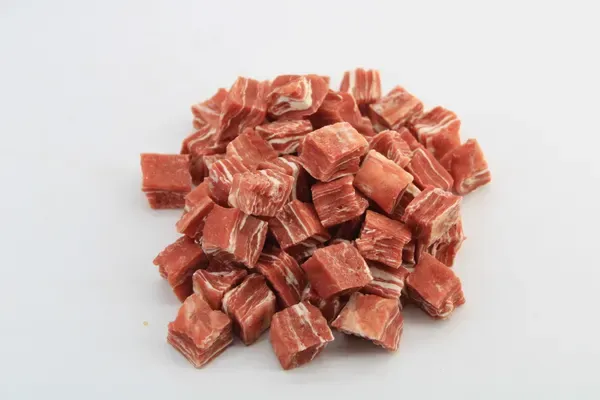 Loose heap of red meat dice treats on a white surface