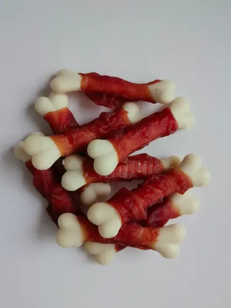 Small knotted rawhide bones wrapped with red meat, scattered on a white surface
